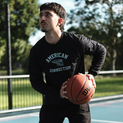 Man holding a basketball on an outdoor court with trees in the background